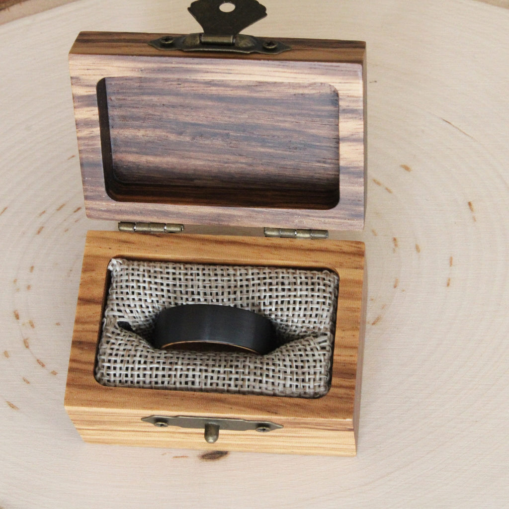 May include: A wooden ring box with a hinged lid and a brass latch. The box is lined with burlap fabric and contains a black ring.