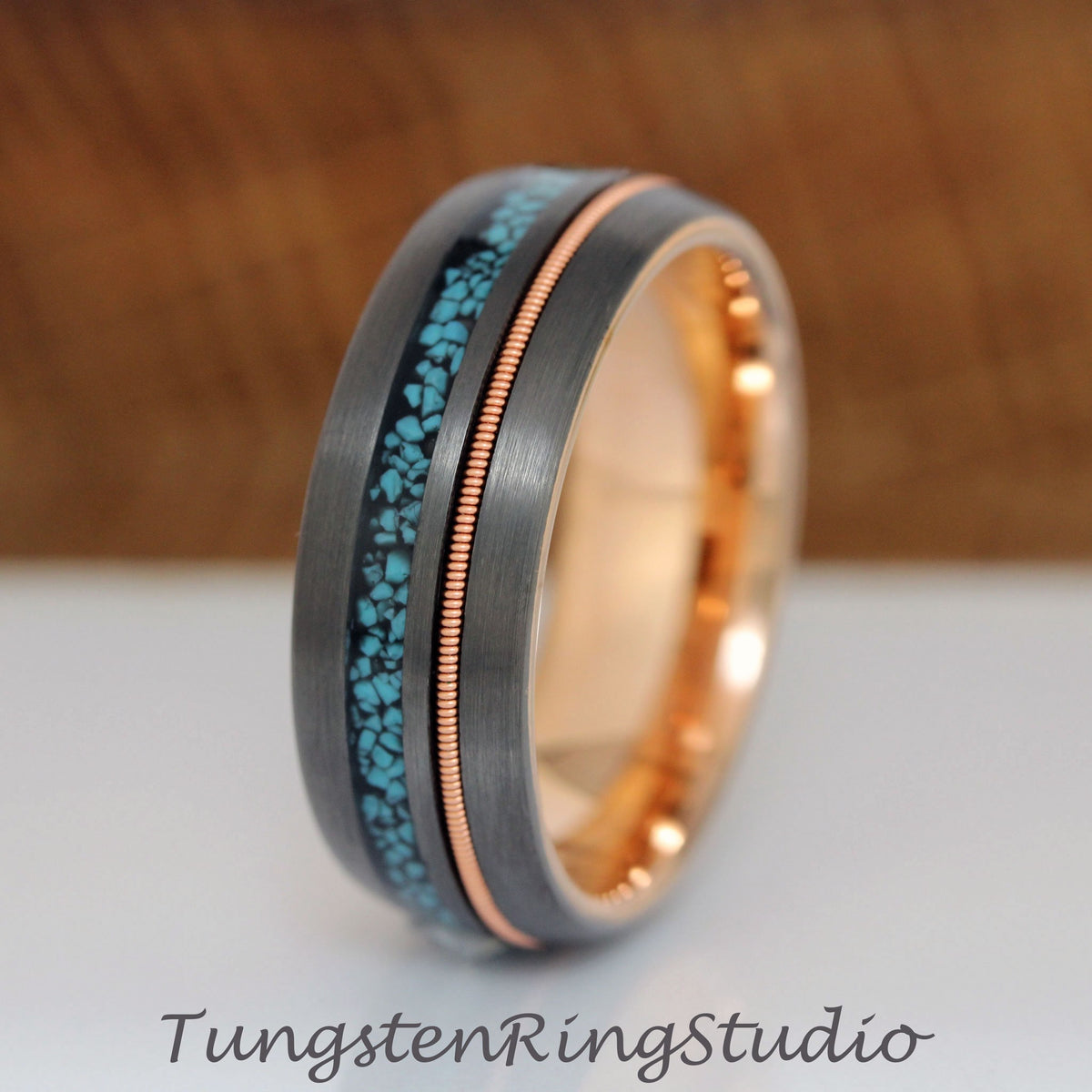 May include: A gray tungsten carbide ring with a thin rose gold band and a turquoise inlay. Tungsten Ring Studio.