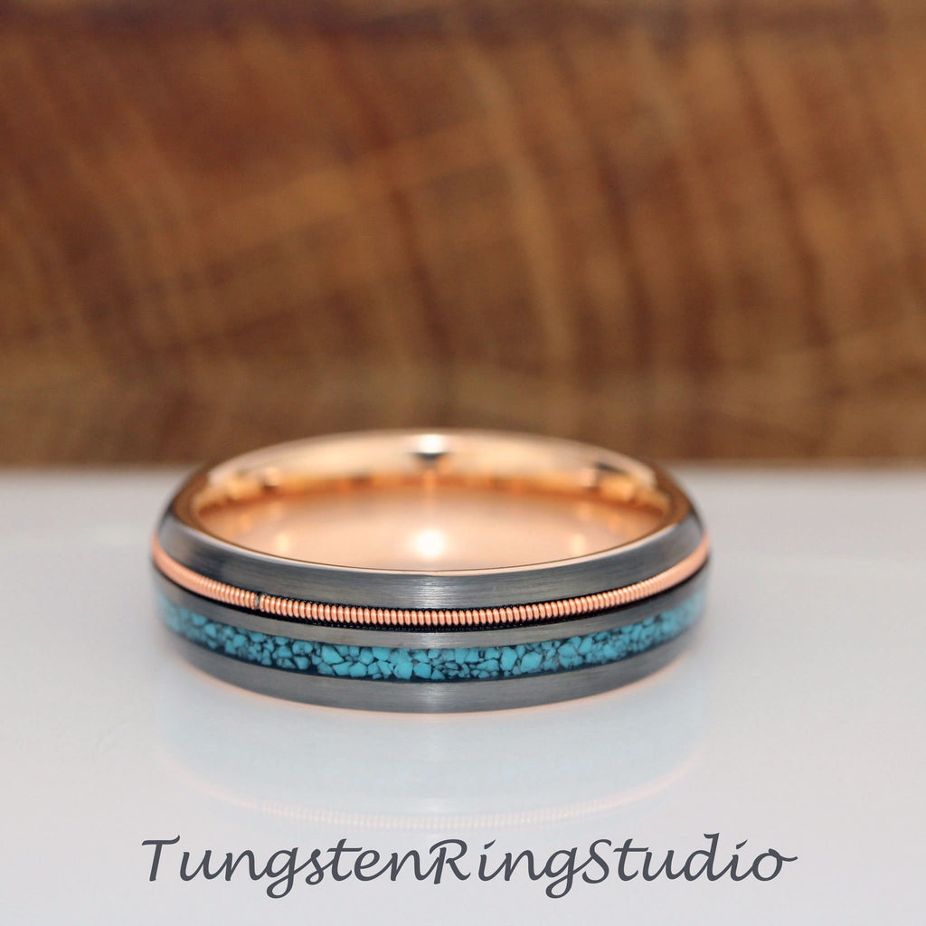 May include: A black tungsten ring with a rose gold inlay and a turquoise inlay. The ring has a brushed finish.