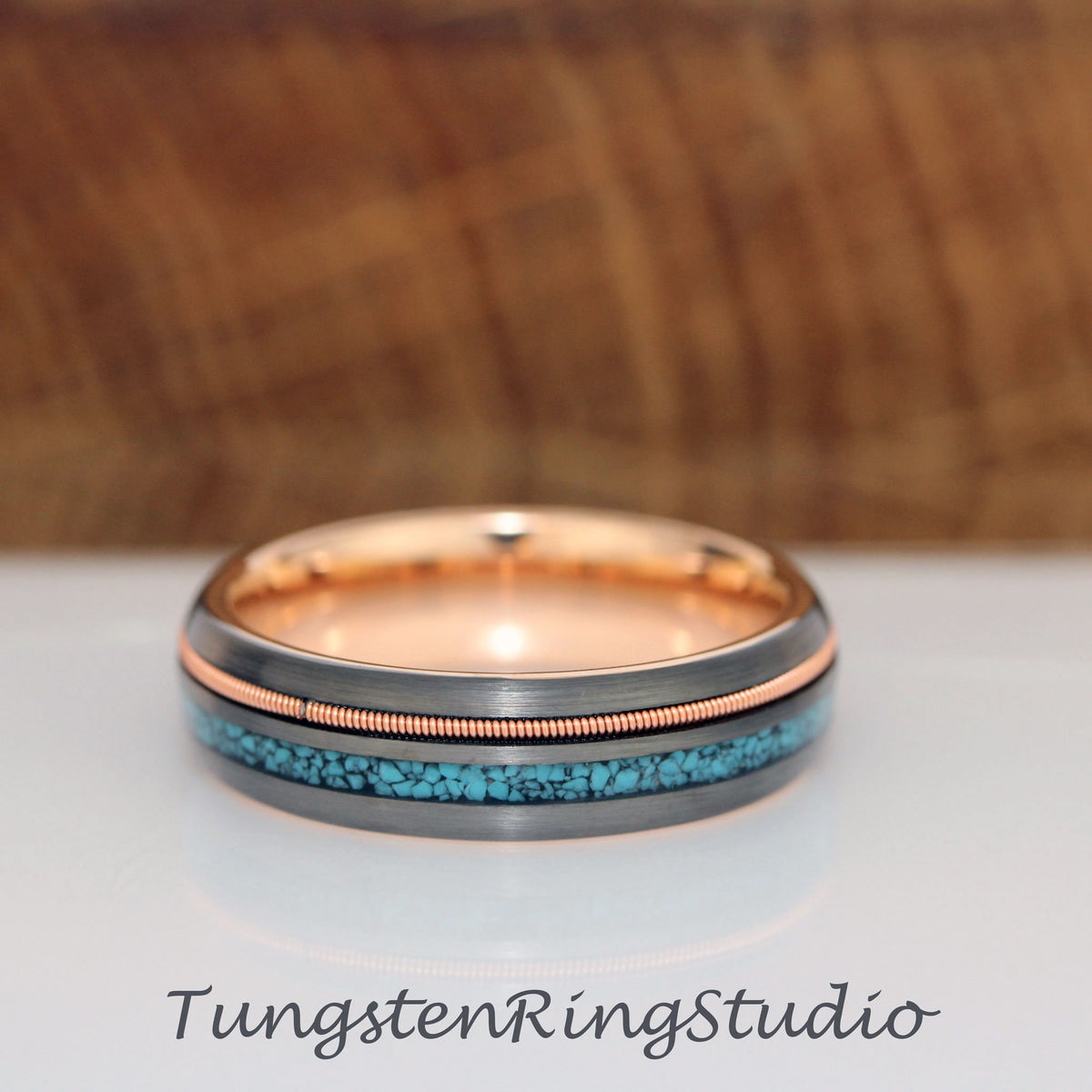 May include: A black tungsten ring with a rose gold inlay and a turquoise inlay. The ring has a brushed finish.