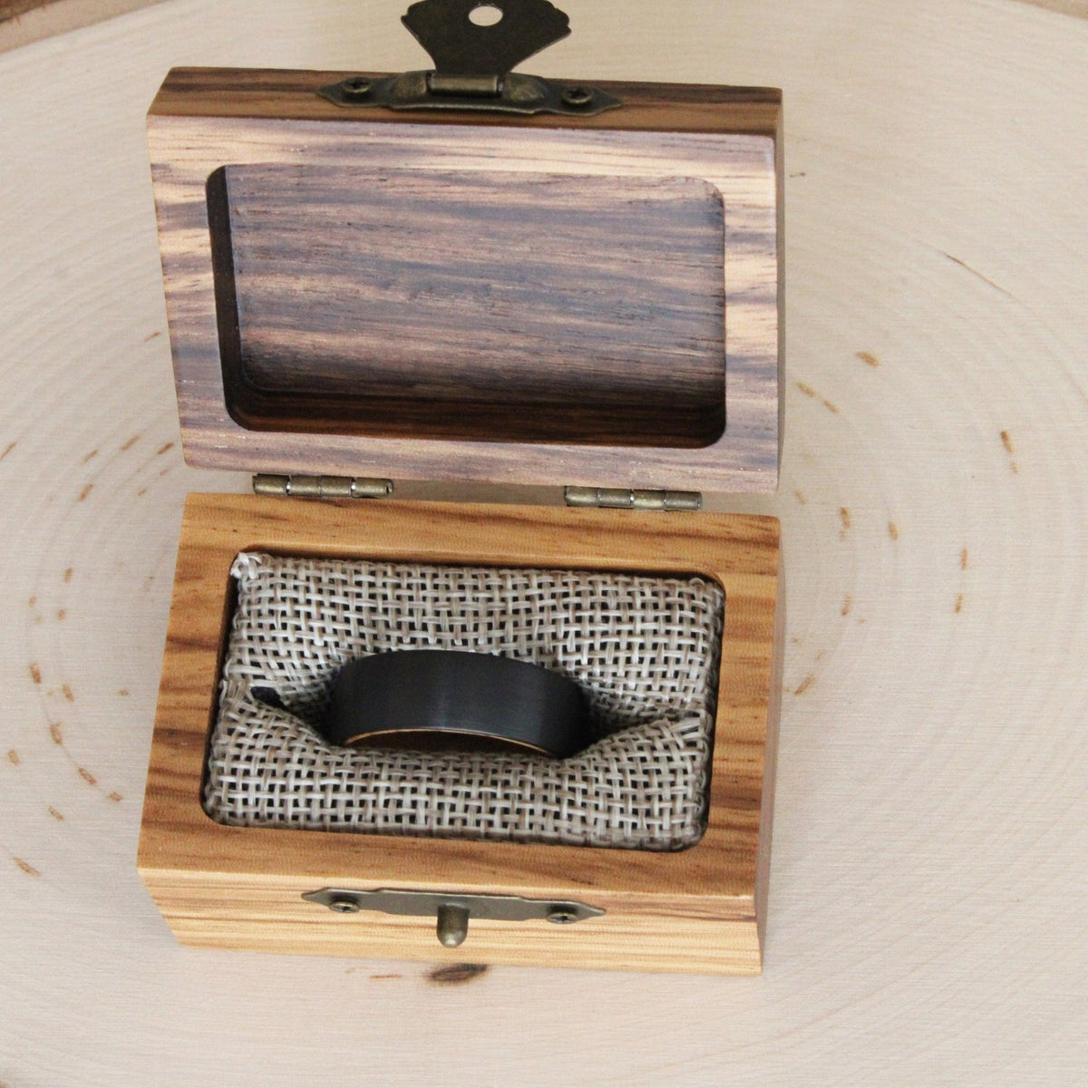 May include: A black ring in a wooden box with a burlap lining. The box has a brass latch and hinges.