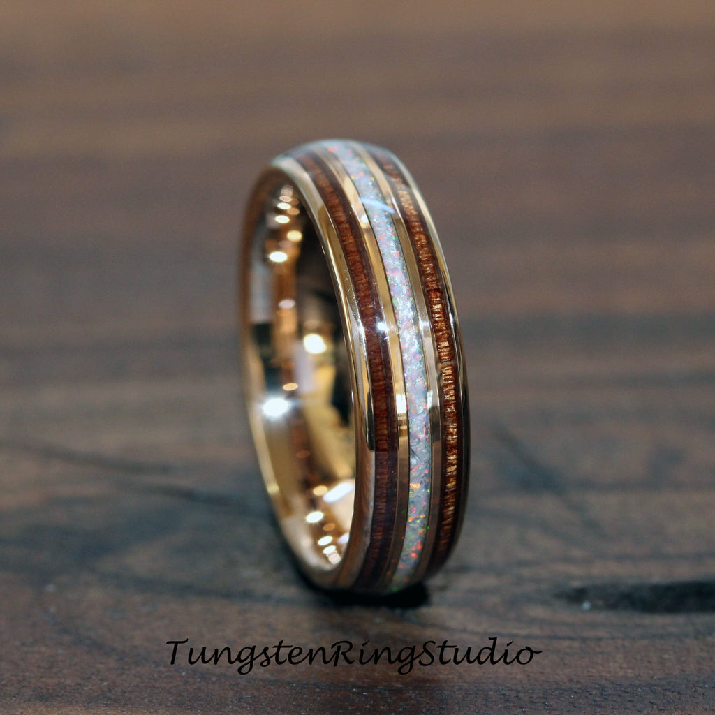 May include: A gold-colored ring with a central band of white opal, flanked by bands of dark wood. The ring has a polished finish and the text "TungstenRingStudio" is visible at the bottom.