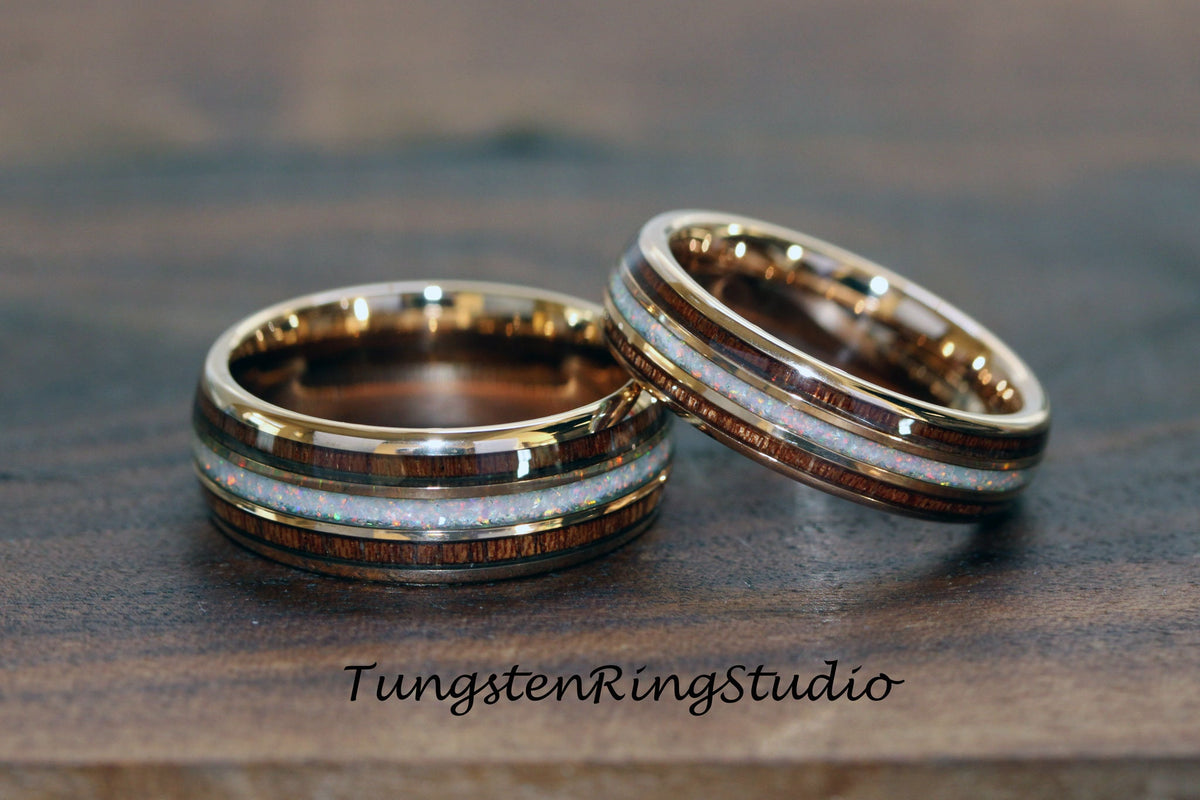May include: Two wedding rings with a gold band, a dark wood inlay, and a white opal center. The rings are displayed on a wooden surface. The text "TungstenRingStudio" is visible at the bottom.