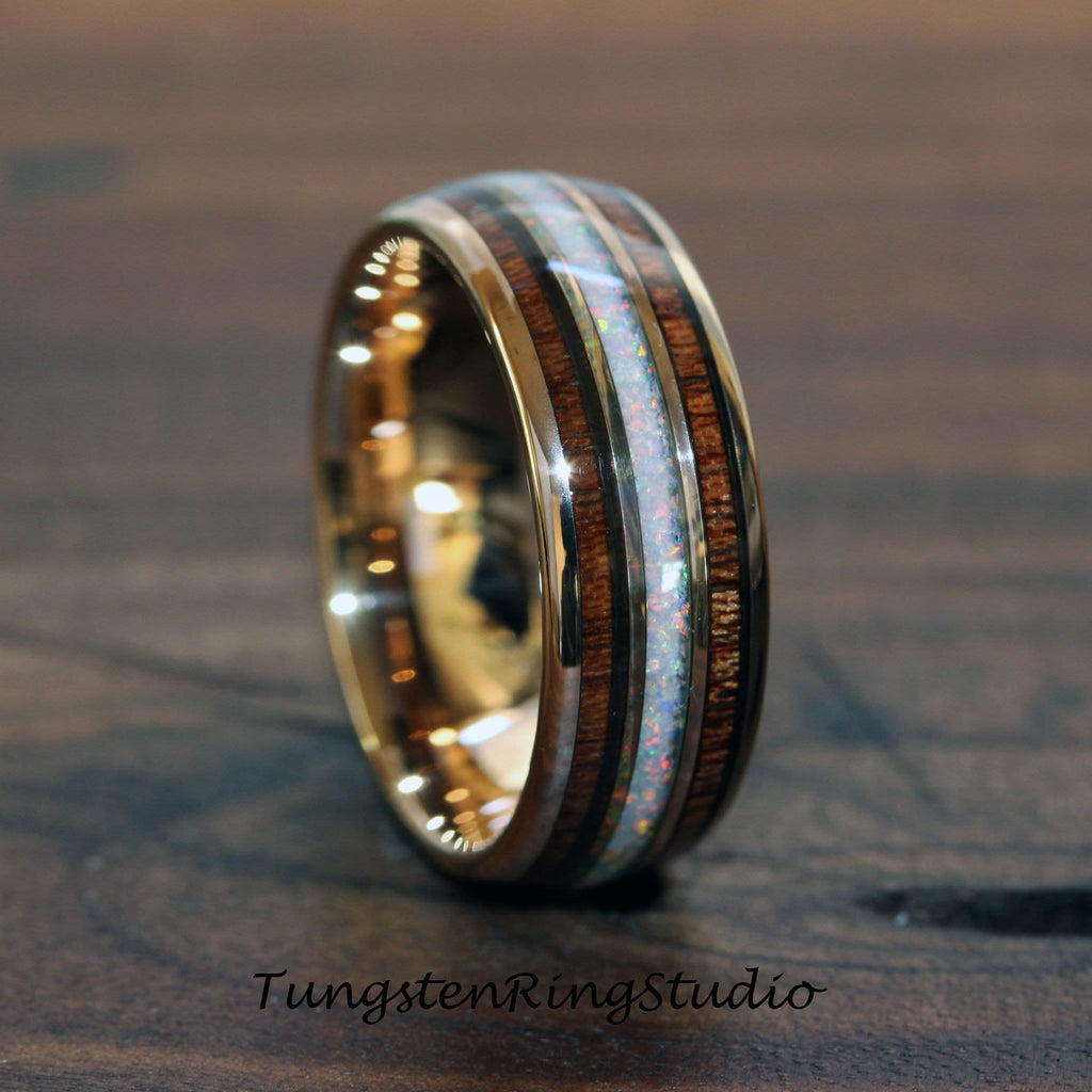 May include: A gold-colored ring with a central band of white opal and flanking bands of dark wood. The ring has a polished finish and a wide band design. The text "TungstenRingStudio" is at the bottom of the image.