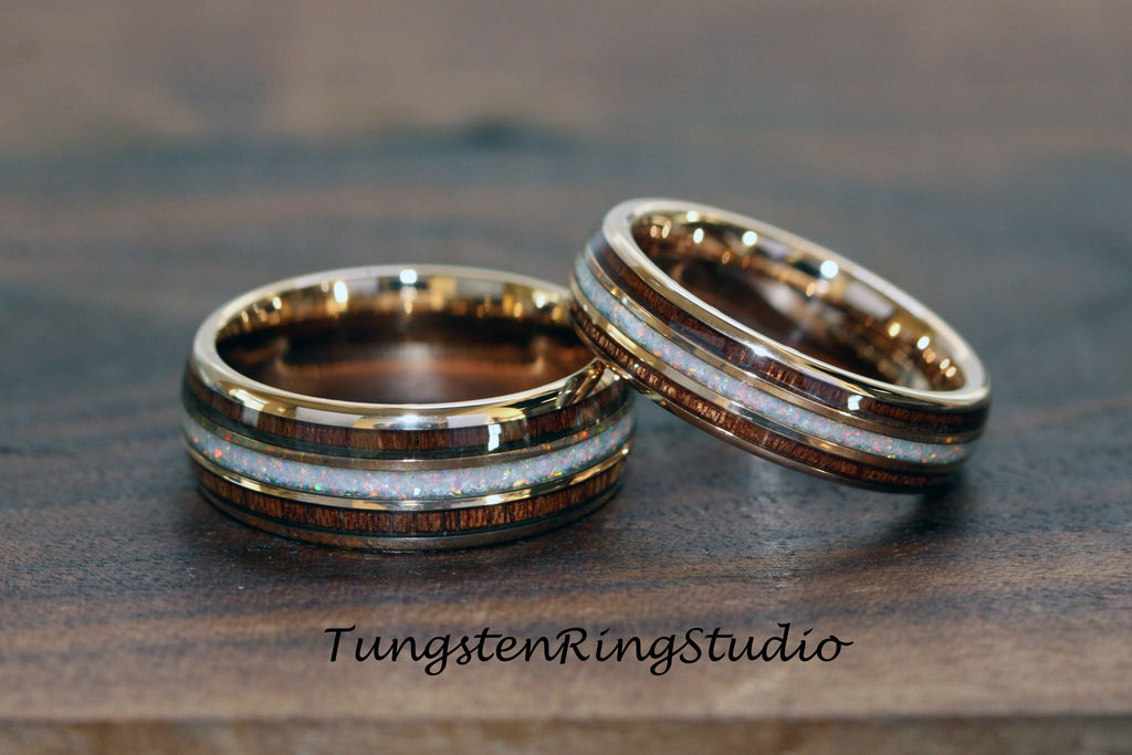 May include: Two wedding rings with a gold band, a dark wood inlay, and a white opal center. The rings are displayed on a wooden surface. The text "TungstenRingStudio" is visible at the bottom.