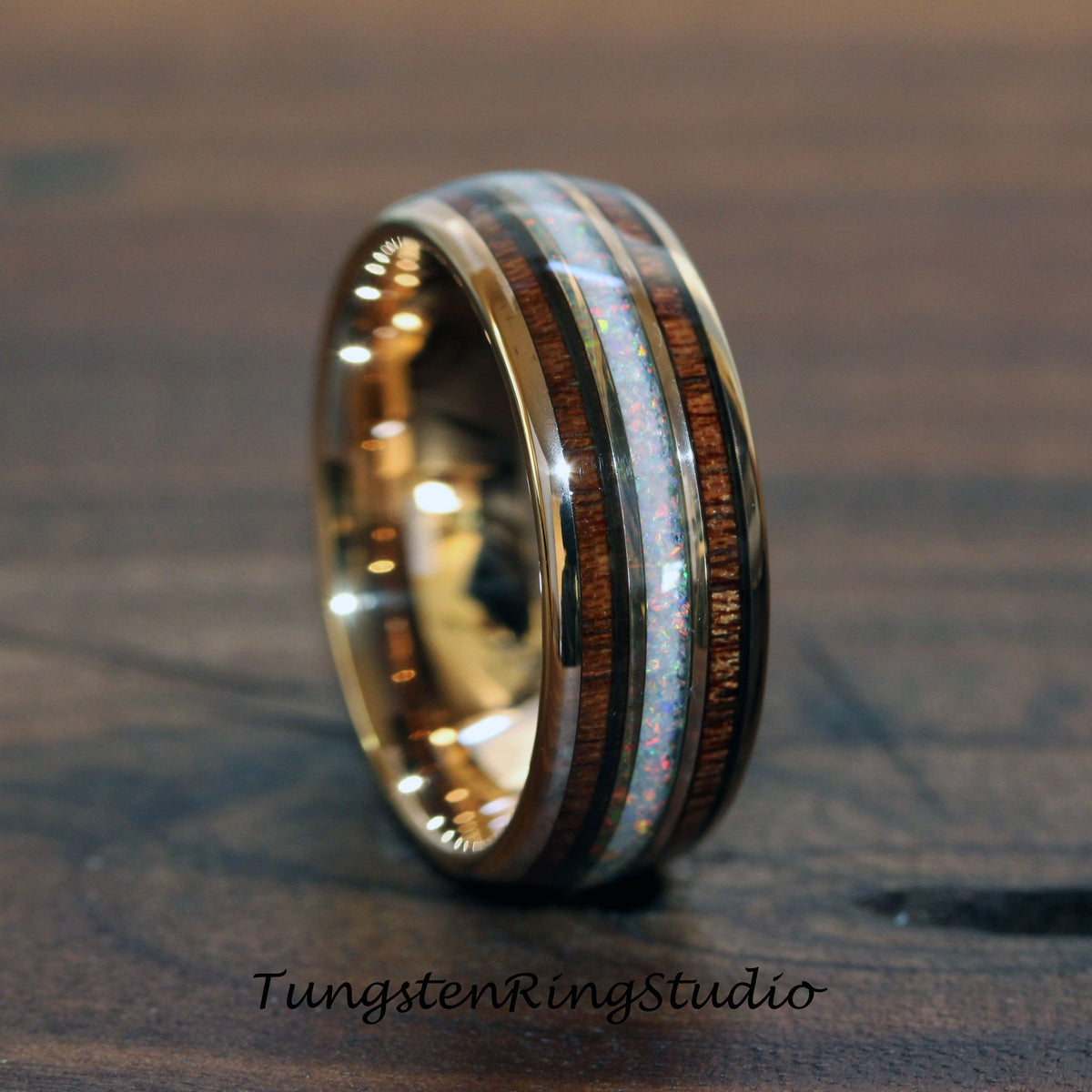 May include: A gold-colored ring with a central band of white opal and flanking bands of dark wood. The ring has a polished finish and a wide band design. The text "TungstenRingStudio" is at the bottom of the image.