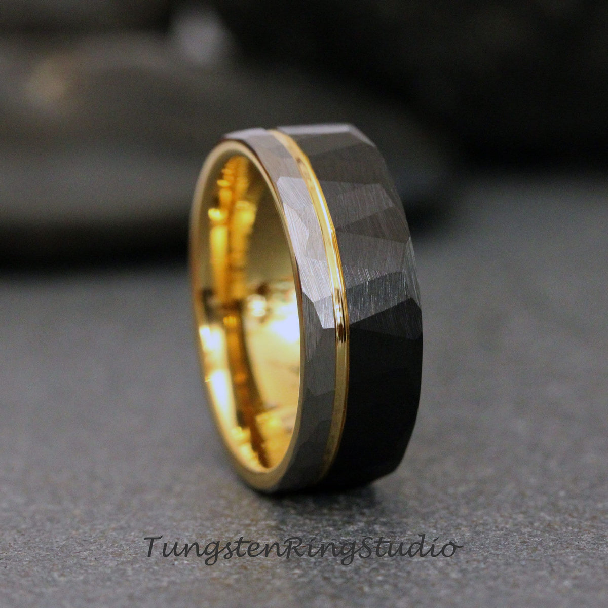 May include: A black tungsten carbide ring with a gold band. The ring has a hammered finish and a beveled edge.