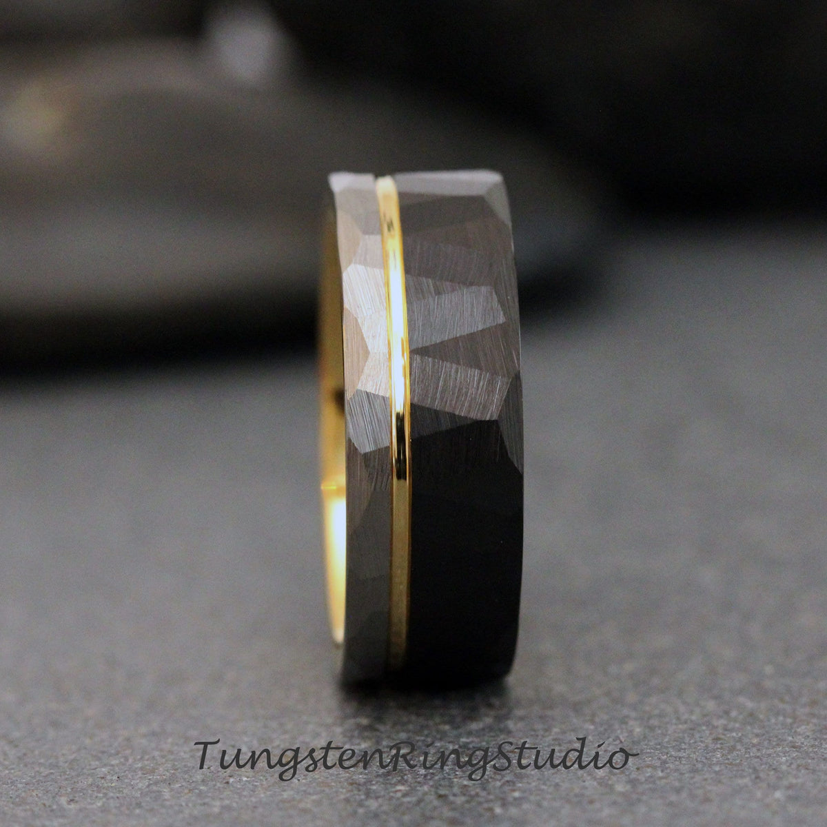 May include: A black tungsten carbide ring with a gold inlay. The ring has a hammered finish and a beveled edge.