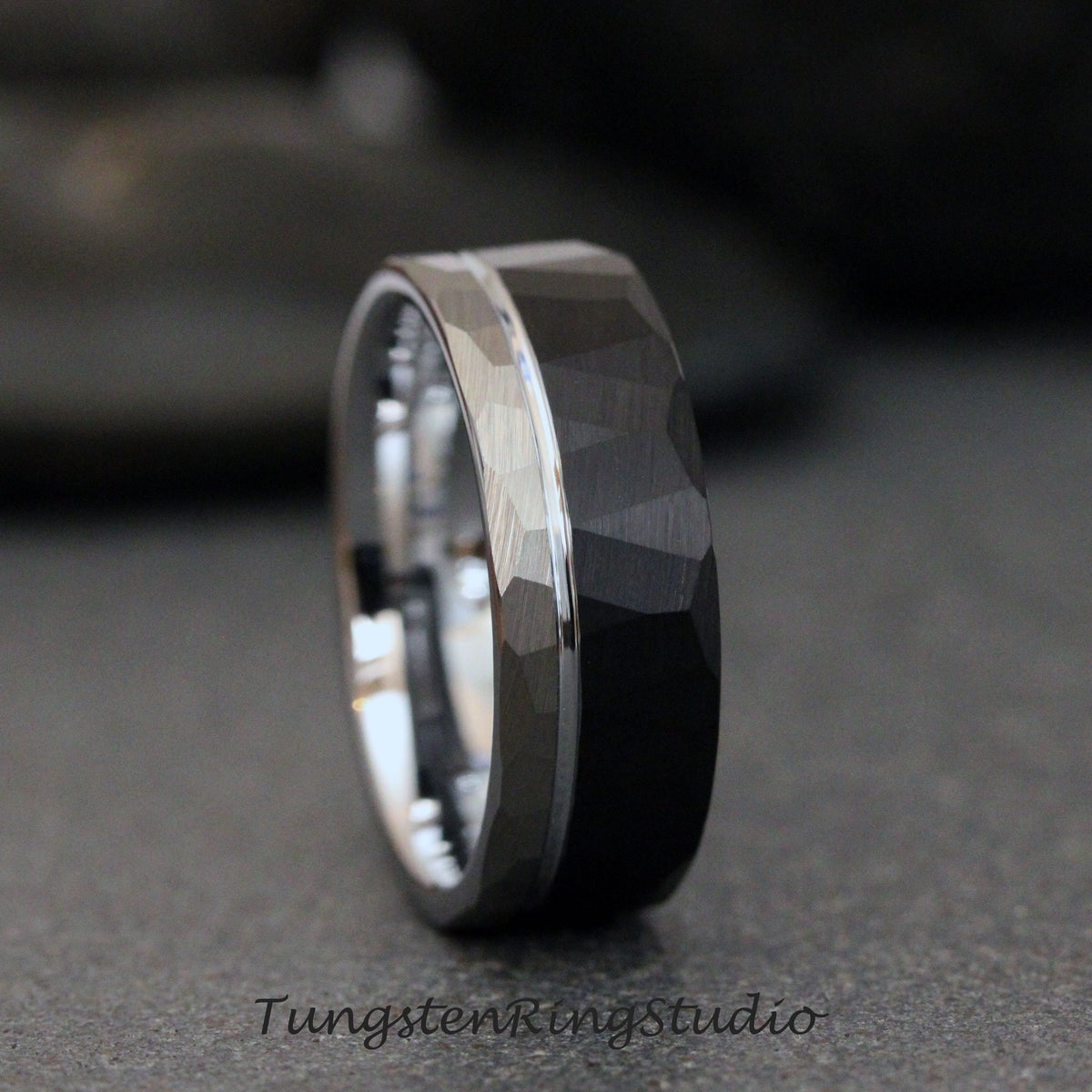 May include: A black tungsten carbide ring with a silver band and a hammered finish. Tungsten Ring Studio.