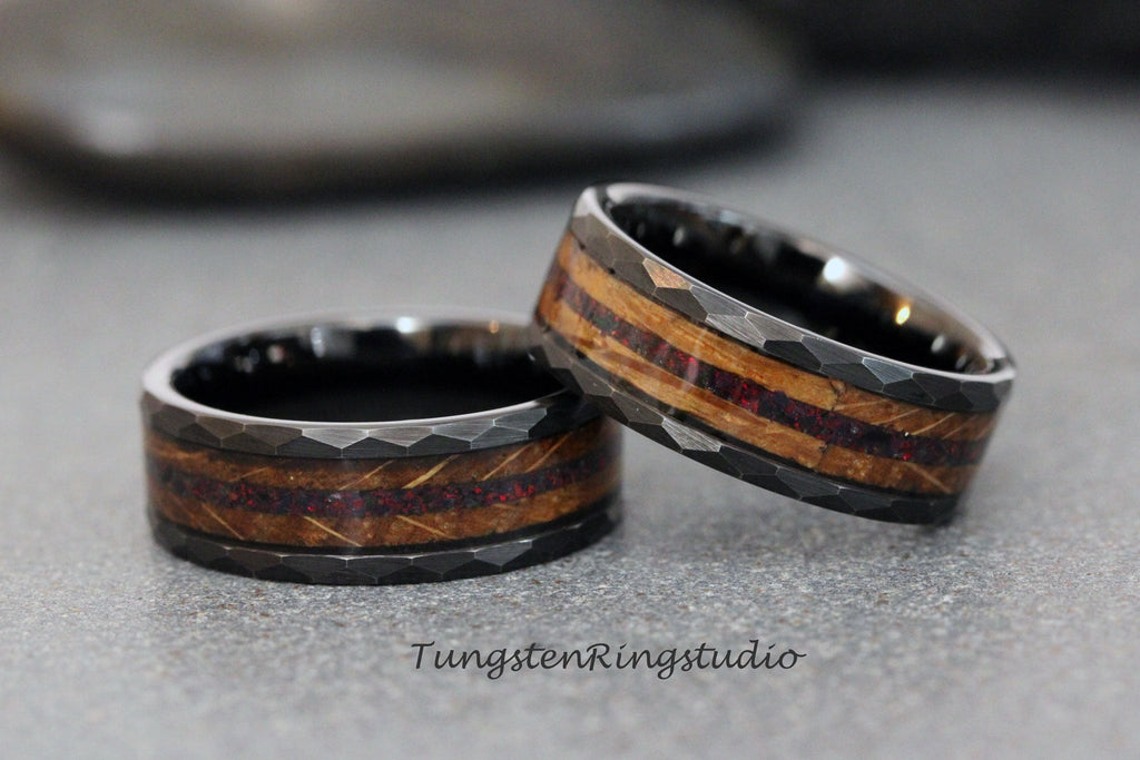 May include: Two black tungsten carbide rings with a hammered finish and a wood inlay with red accents. The rings are stacked on top of each other.