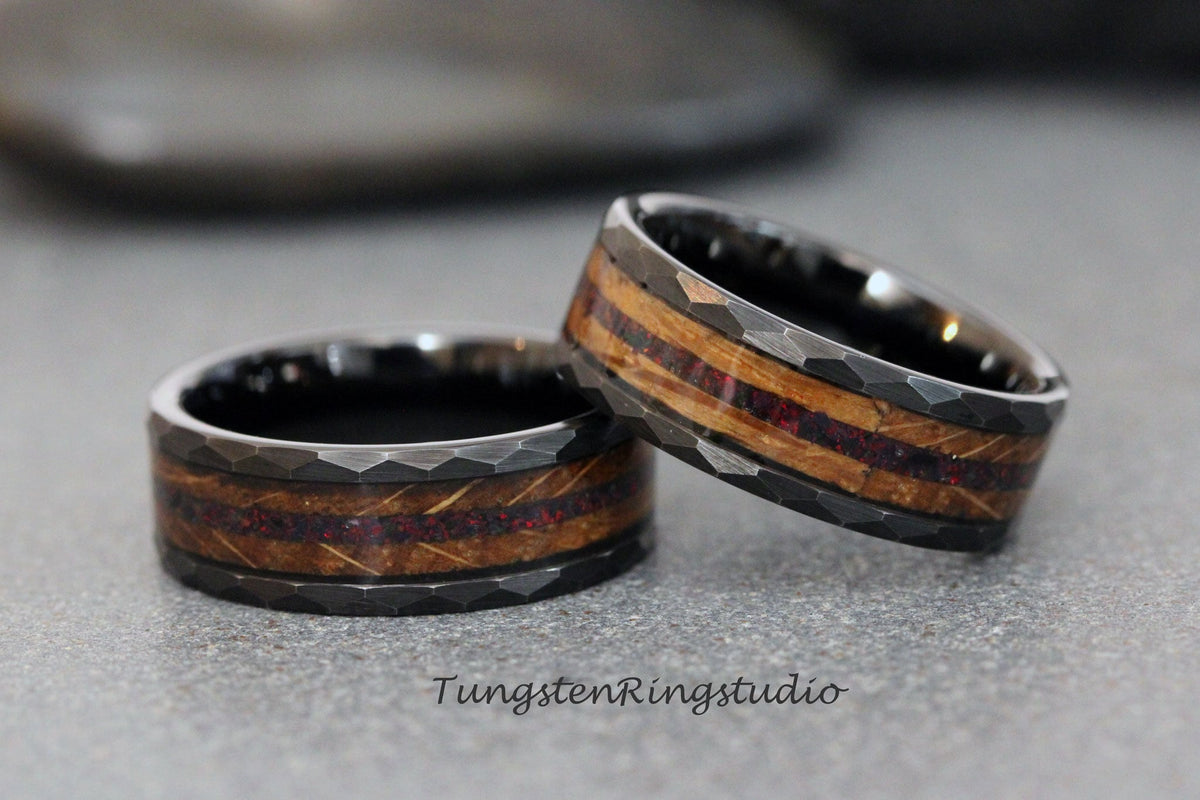 May include: Two black tungsten carbide rings with a hammered finish and a wood inlay with red accents. The rings are stacked on top of each other.
