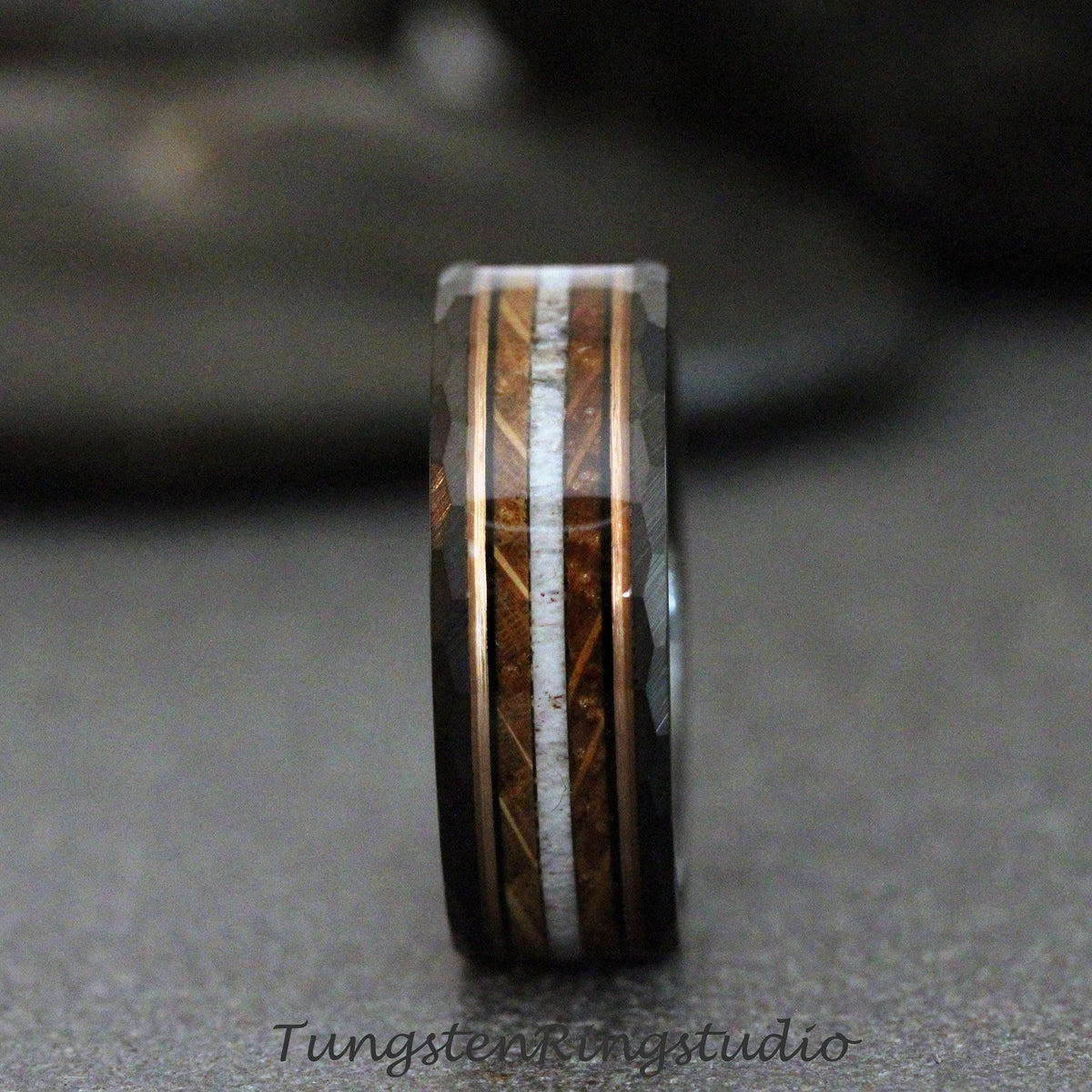May include: A black tungsten ring with a rose gold inlay and a wood and white bone inlay. The ring has a beveled edge.