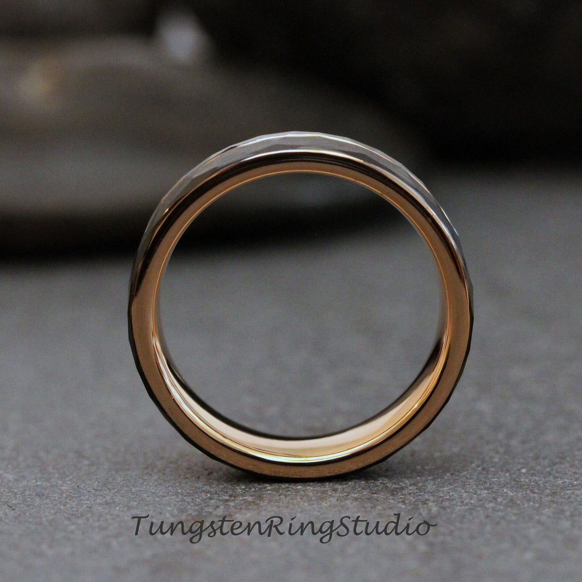May include: A close-up of a rose gold tungsten carbide ring with a hammered finish. The ring is on a gray surface.