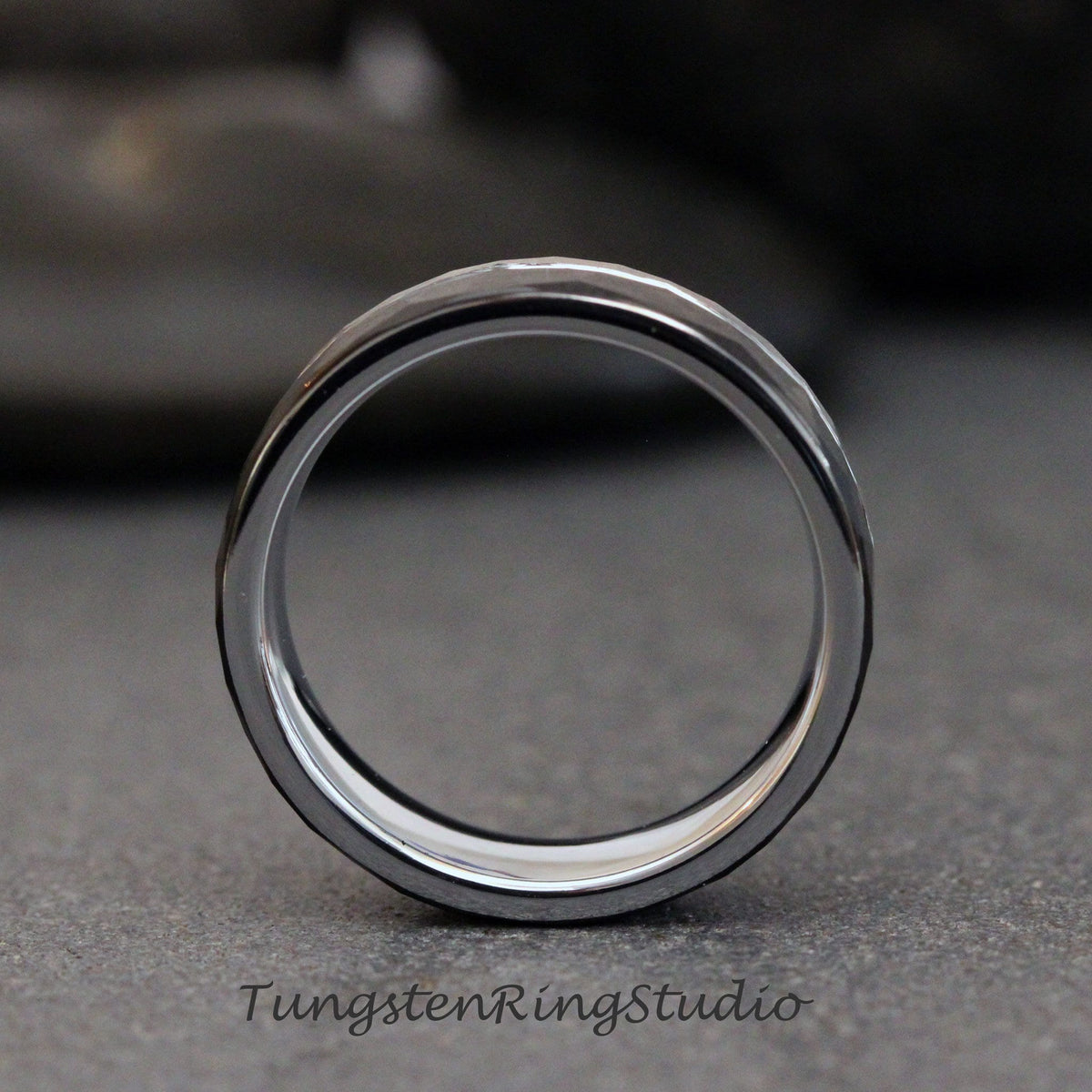 May include: A silver tungsten carbide ring with a hammered finish. The ring is shown from the side, with the inside of the ring facing the viewer.