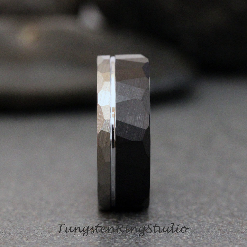 May include: A black tungsten carbide ring with a hammered finish and a silver band. The ring has a beveled edge and a polished finish.
