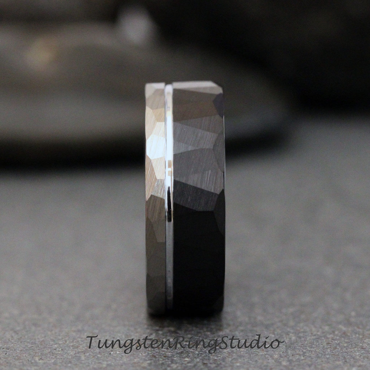 May include: A black tungsten carbide ring with a hammered finish and a silver band. The ring has a beveled edge and a polished finish.