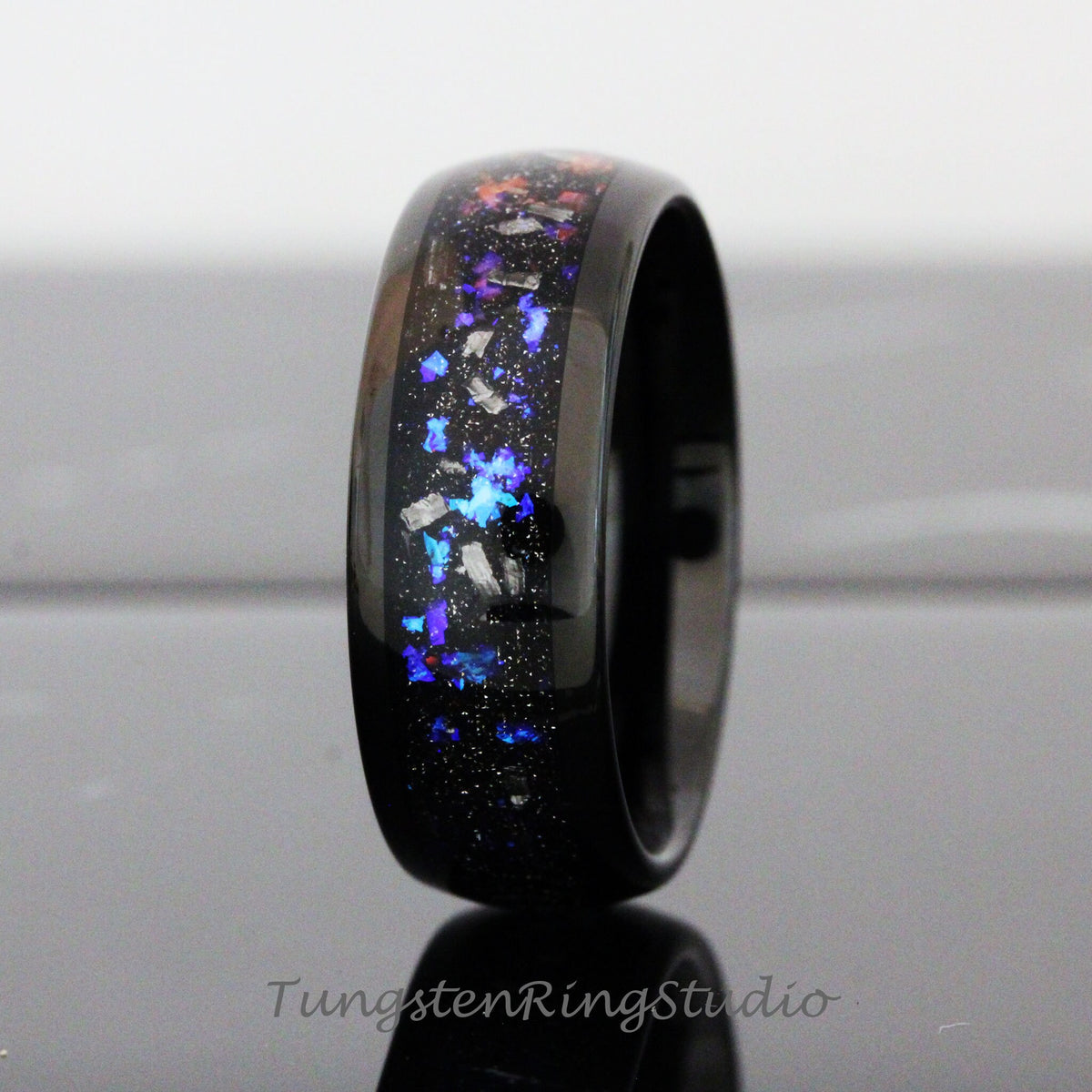 May include: A black tungsten ring with a blue, purple, and orange glitter inlay. The ring is polished and has a beveled edge.