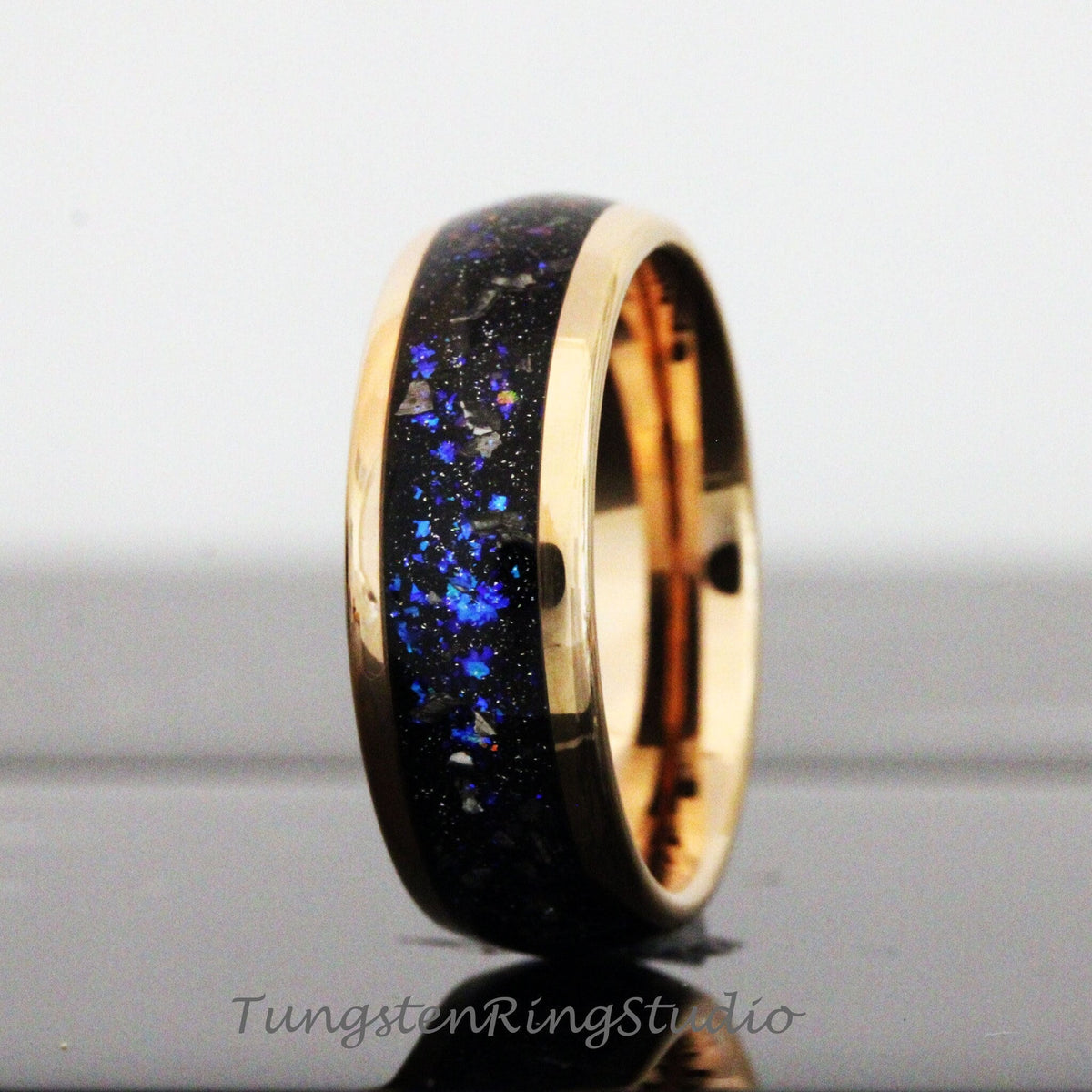 May include: A black and blue tungsten carbide ring with a rose gold band. The ring has a unique design with blue and black flecks throughout the band.