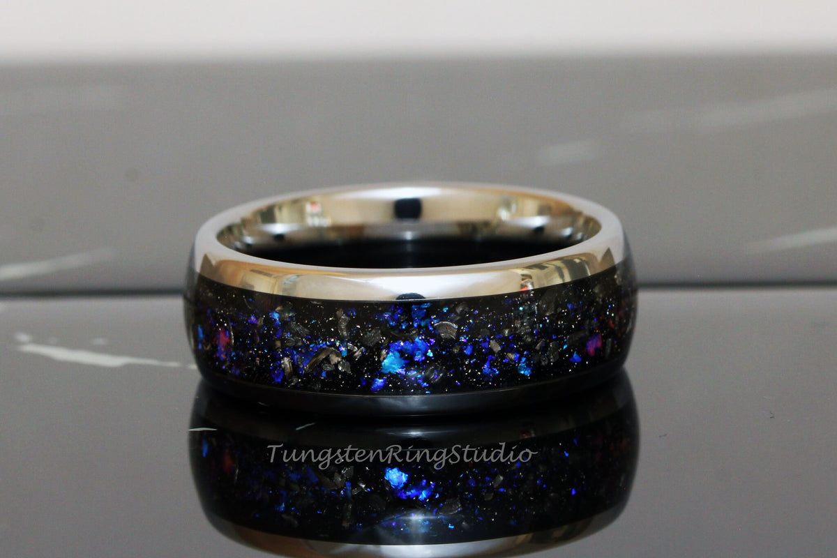 May include: A black tungsten ring with a silver band and a blue and black inlay. The inlay is made of crushed meteorite and has a sparkly appearance.