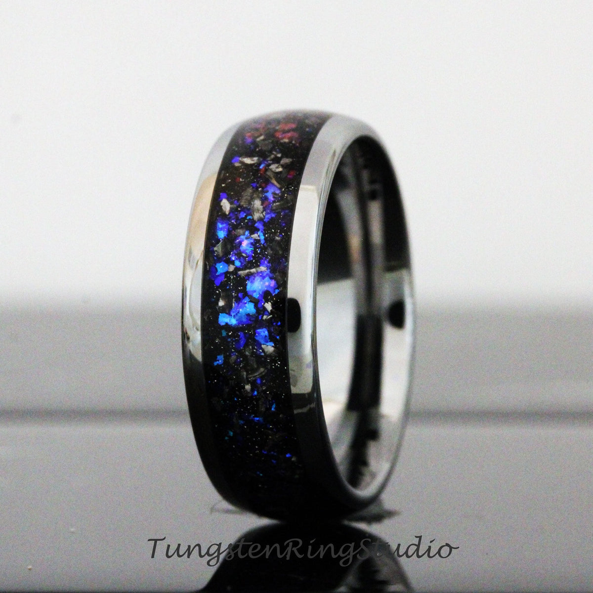 May include: A black tungsten carbide ring with a blue and silver inlay. The ring has a polished finish and a beveled edge.