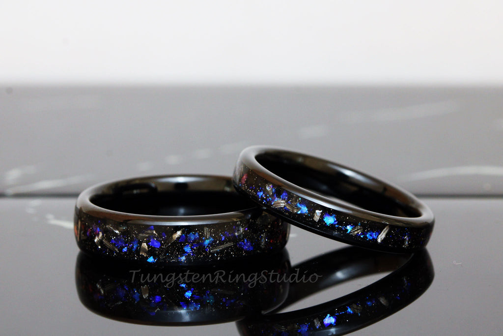 May include: Two black tungsten carbide rings with blue and silver glitter embedded in the black polished surface. The rings are stacked on top of each other.