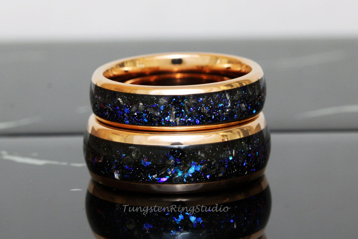 May include: Two rose gold tungsten carbide rings with a black and blue glitter inlay. The rings are stacked on top of each other.