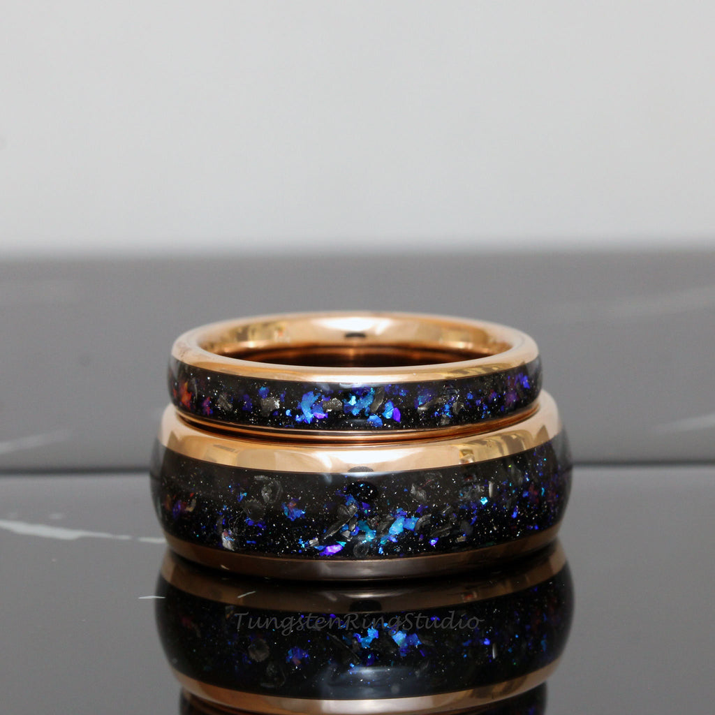 May include: Two rose gold tungsten carbide rings with a black and blue glitter inlay. The rings are stacked on top of each other.