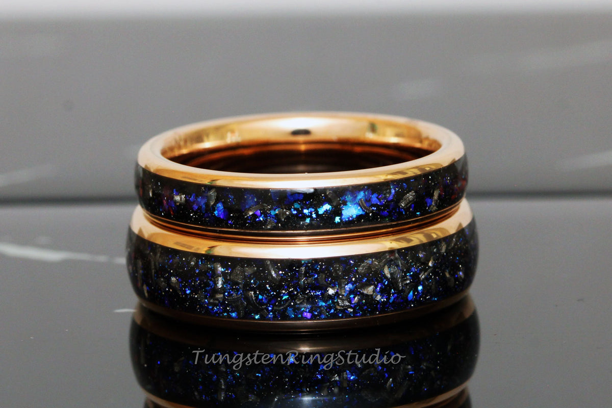May include: Two gold tungsten carbide rings with a black and blue galaxy inlay. The rings are stacked on top of each other.