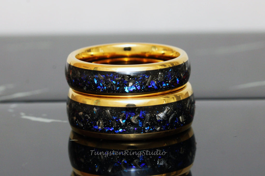 May include: Two gold tungsten carbide rings with a black inlay and blue glitter. The rings are stacked on top of each other.