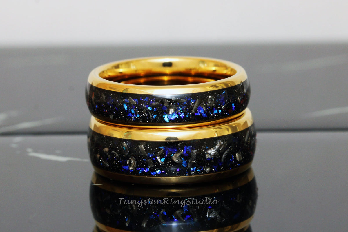 May include: Two gold tungsten carbide rings with a black inlay and blue glitter. The rings are stacked on top of each other.