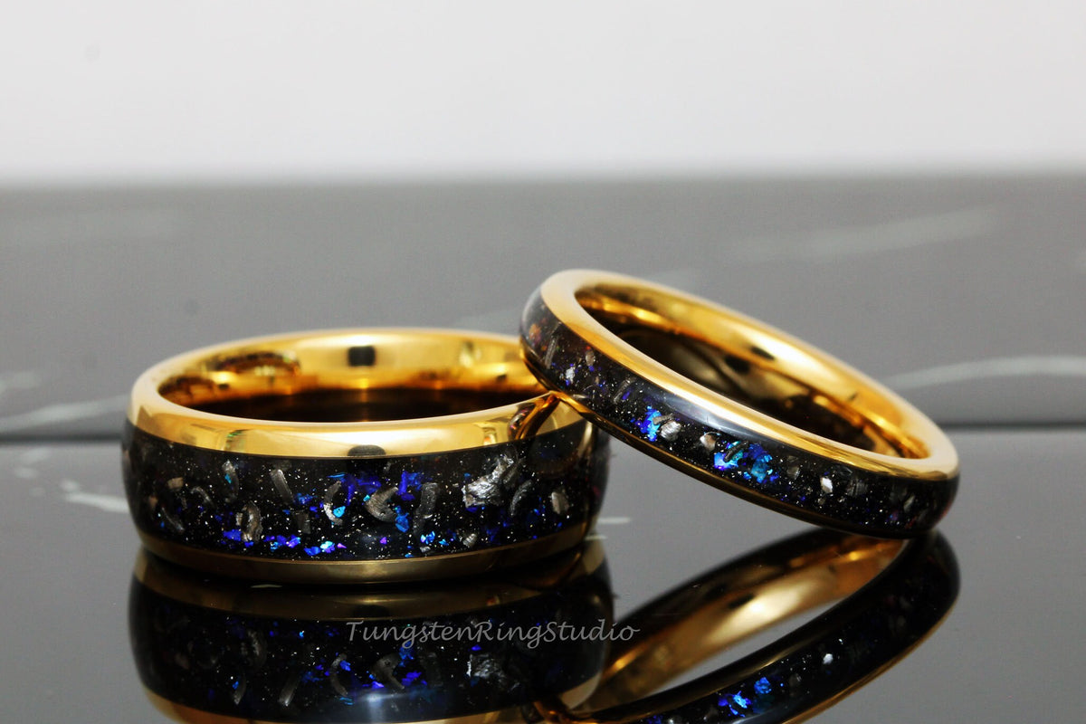 May include: Two gold tungsten carbide rings with a black inlay and blue glitter. The rings are stacked on top of each other.