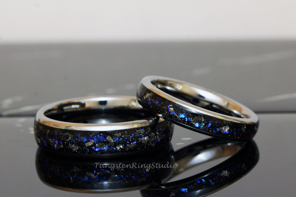 May include: Two black tungsten carbide rings with a silver band and blue glitter embedded in the black surface. The rings are stacked on top of each other.