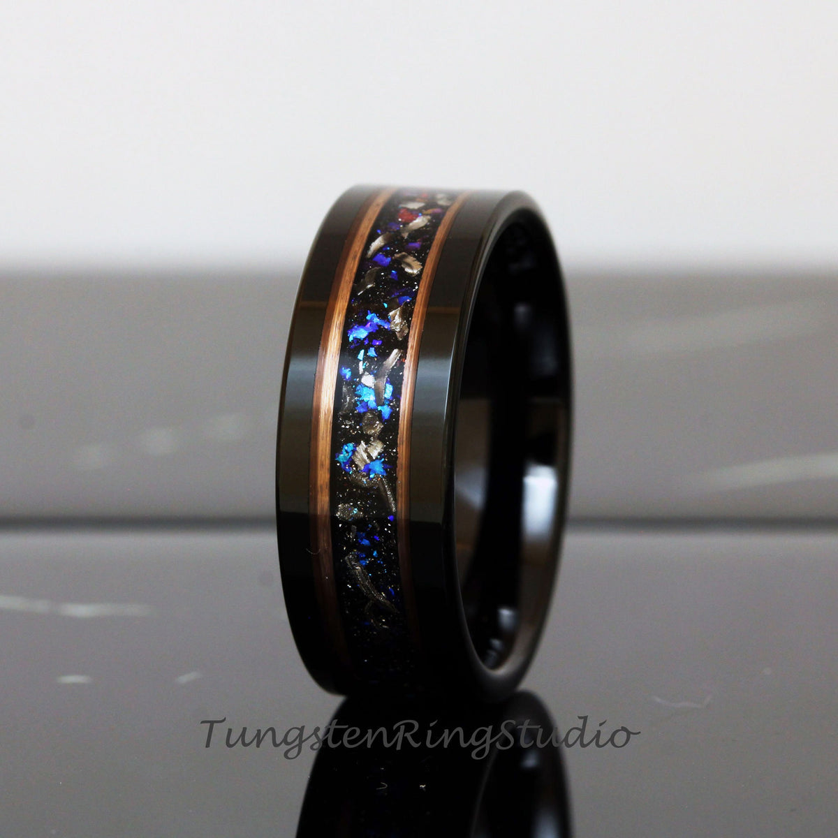 May include: A black tungsten ring with a copper and blue inlay. The inlay features a scattered pattern of blue and copper flecks.