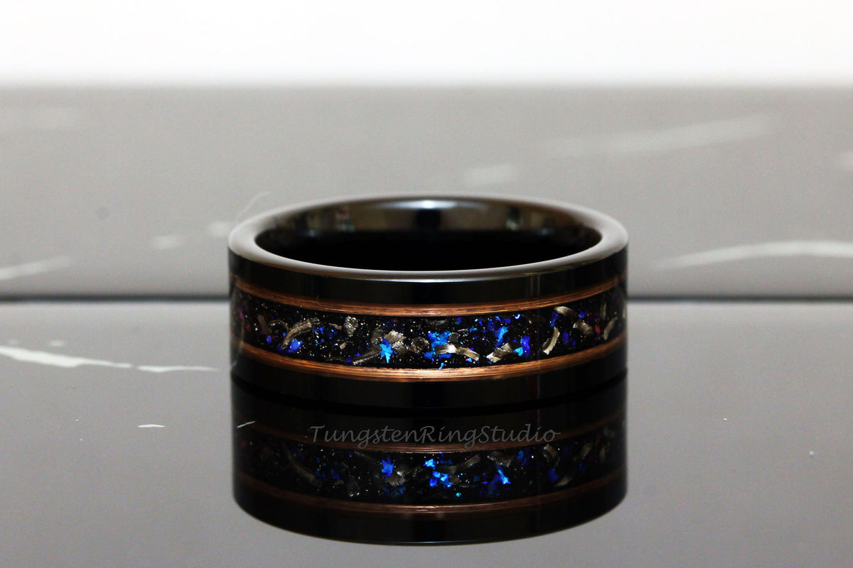 May include: Black tungsten ring with a copper inlay and blue and silver glitter. The ring is on a reflective surface. TungstenRingsStudio is visible on the ring.