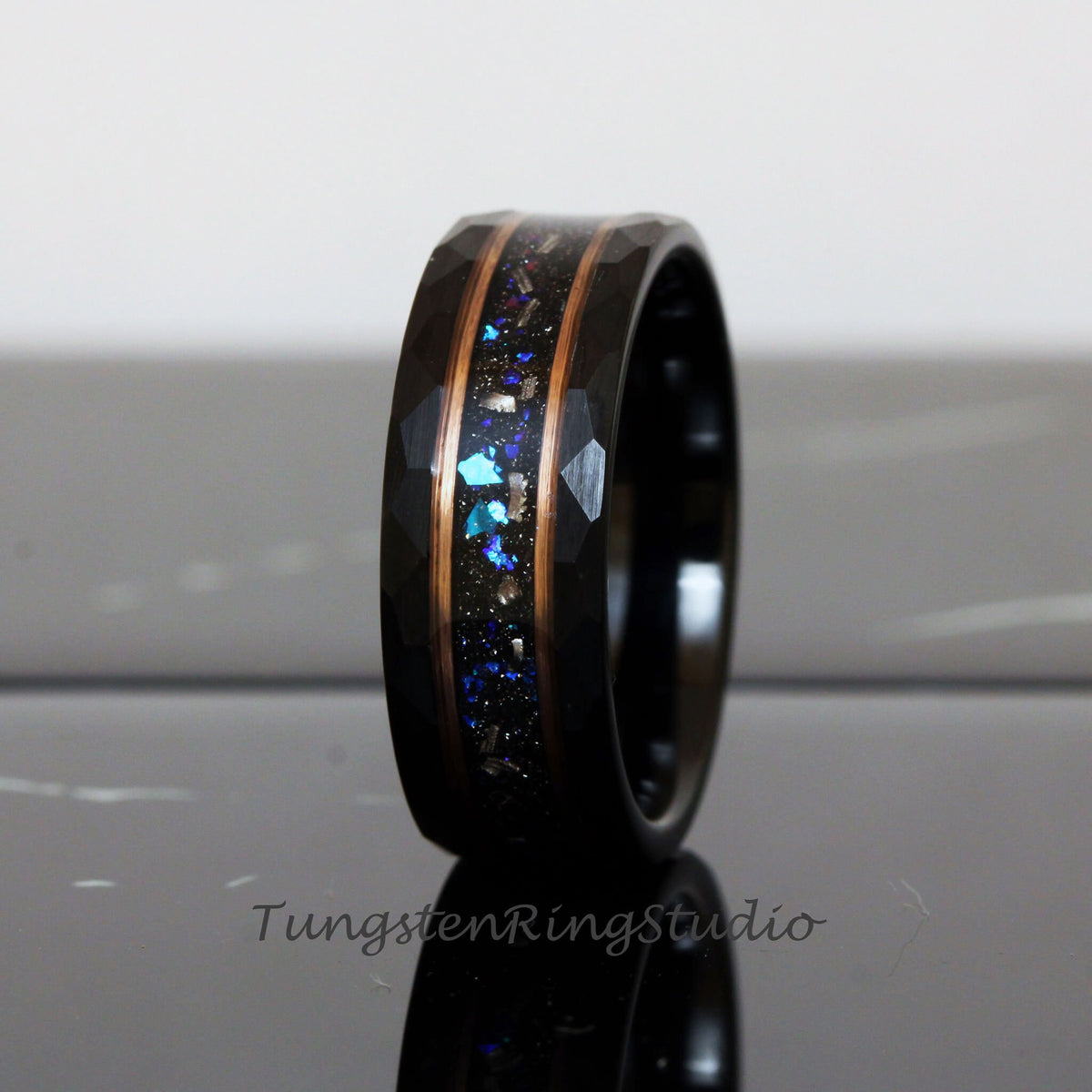 May include: Black tungsten carbide ring with a hammered finish and a copper inlay. The inlay is filled with blue and silver glitter.