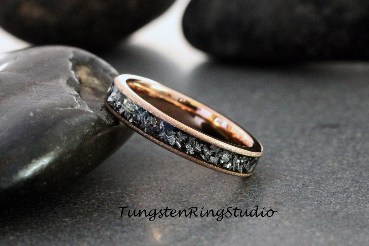 May include: Rose gold ring with a band of dark gray, irregularly shaped stones. The ring is set against a dark background, with the text "TungstenRingStudio" visible in the lower right corner.