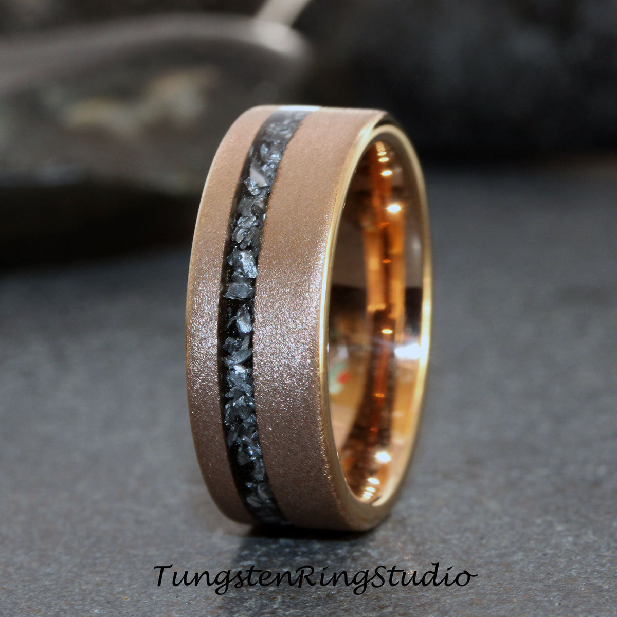May include: A brushed rose gold tungsten carbide ring with a black inlay of small stones. The ring has a beveled edge and a polished finish.