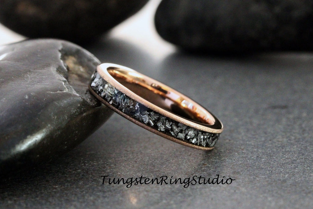 May include: A rose gold tungsten carbide ring with a black meteorite inlay. The ring is shown on a gray background.