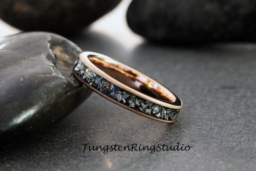 May include: A rose gold tungsten carbide ring with a black meteorite inlay. The ring is shown on a gray background.