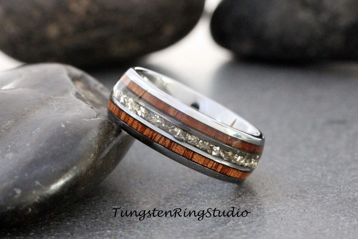 May include: A silver tungsten ring with a brown wood inlay and a row of silver accents. TungstenRingStudio.