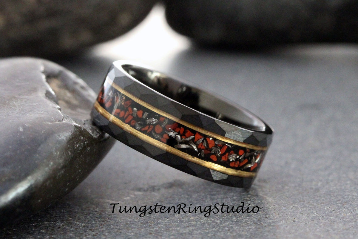 May include: A black tungsten carbide ring with a gold inlay and red and black meteorite inlay. The ring has a beveled edge and a brushed finish.