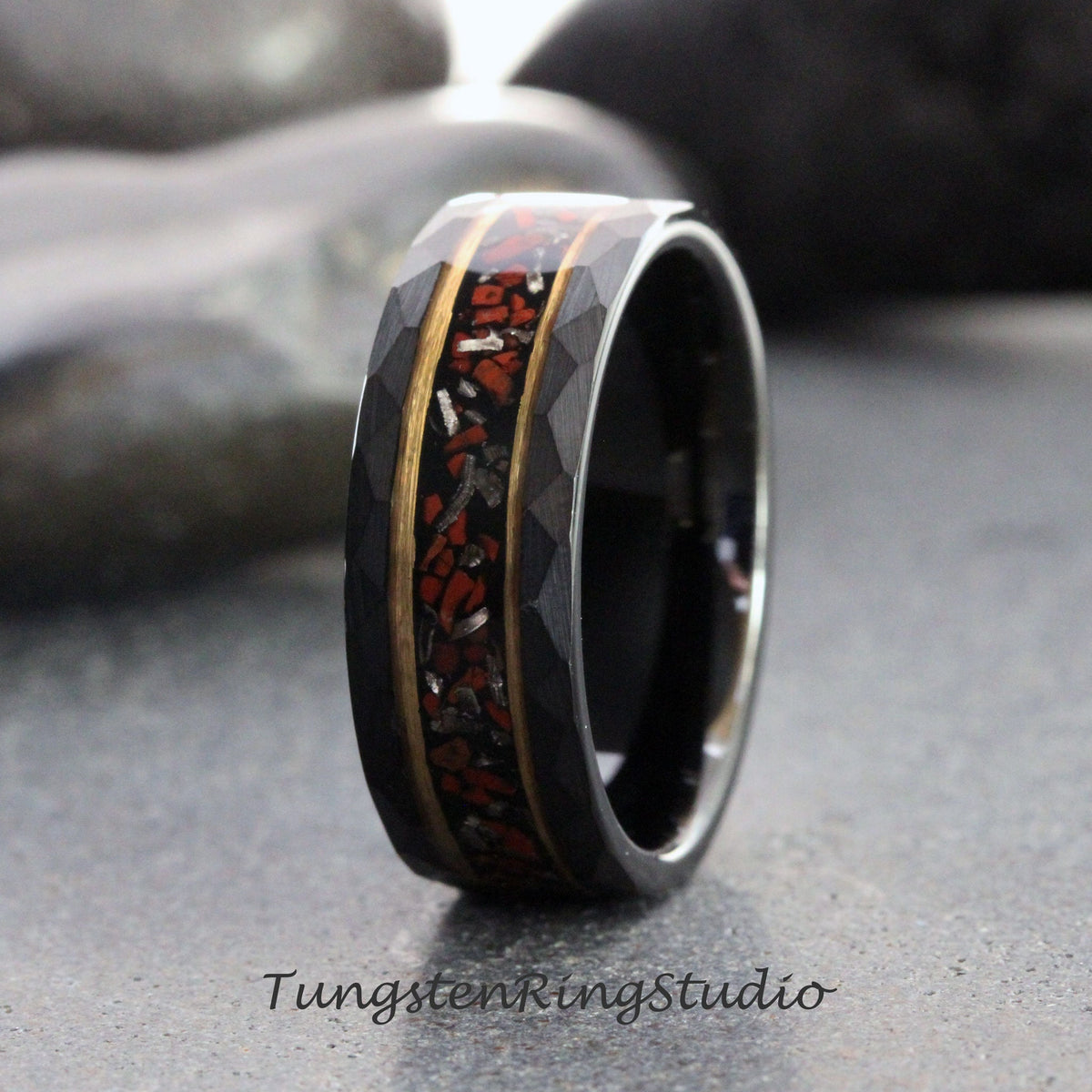 May include: A black tungsten carbide ring with a red and gold inlay. The ring has a hammered finish and a beveled edge.