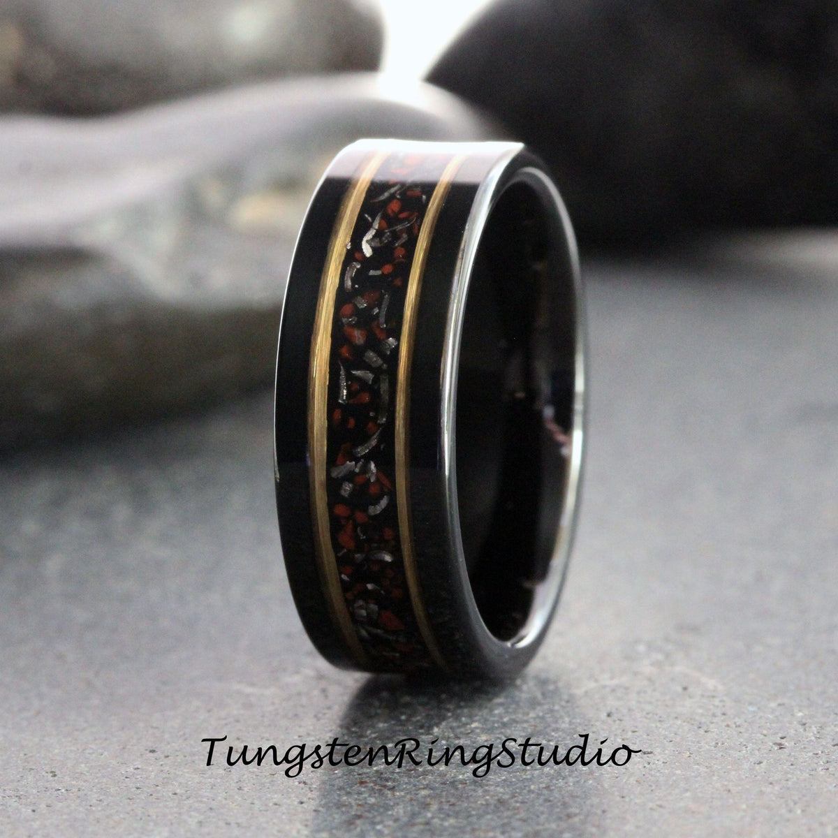 May include: Black tungsten carbide ring with a red and gold inlay. The inlay has a unique pattern and is set into the ring.