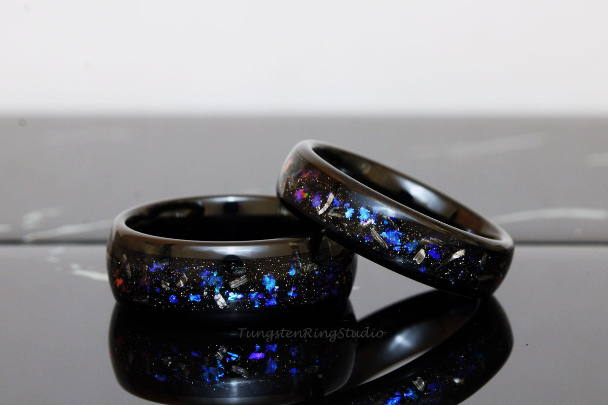 May include: Two black tungsten carbide rings with a galaxy-inspired design. The rings are embedded with blue, silver, and black glitter.