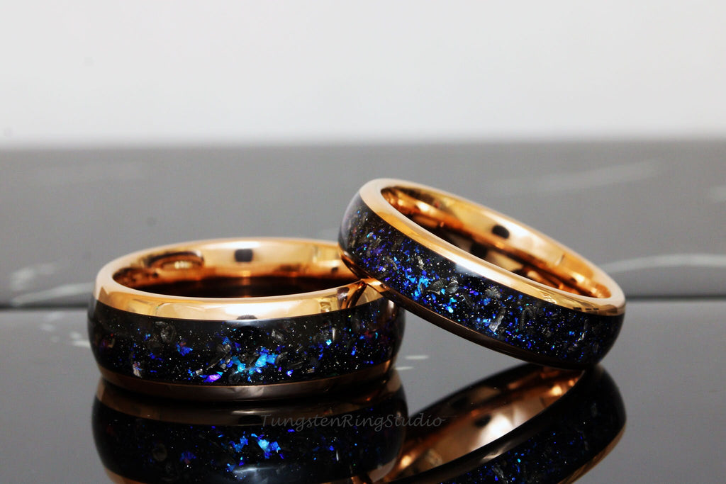 May include: Two matching tungsten carbide rings with a black inlay and a rose gold band. The inlay has a sparkly blue and black pattern.