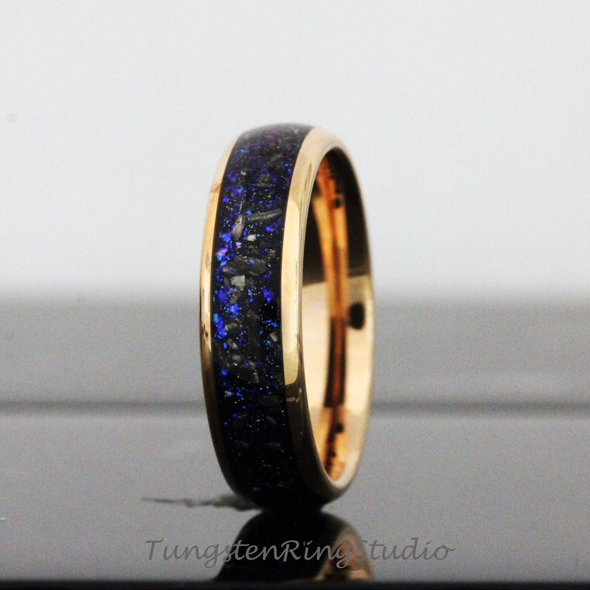 May include: A gold tungsten carbide ring with a blue and black inlay. The ring has a polished finish and a beveled edge.