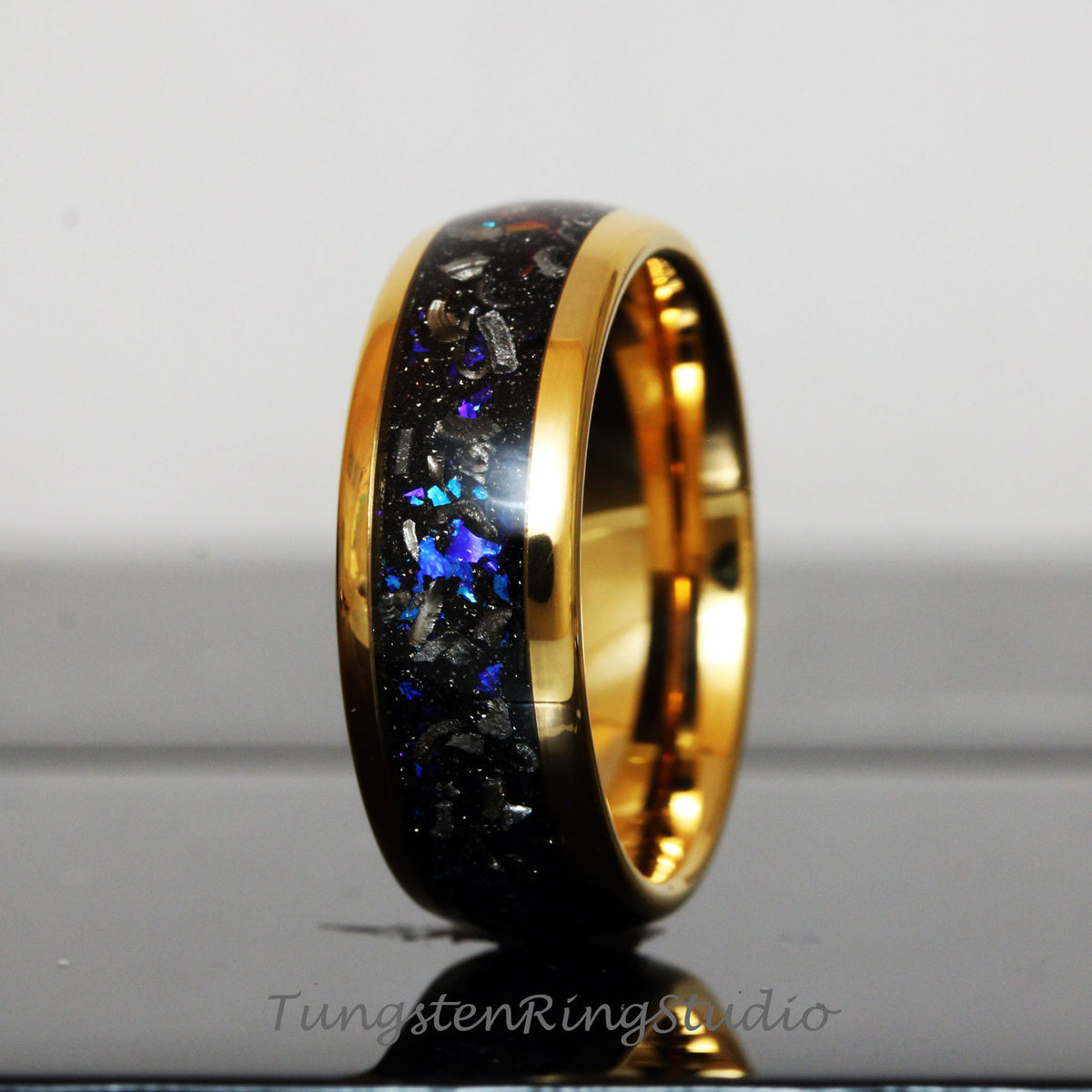 May include: A gold and black tungsten carbide ring with a blue and silver inlay. The ring has a polished finish and a beveled edge.