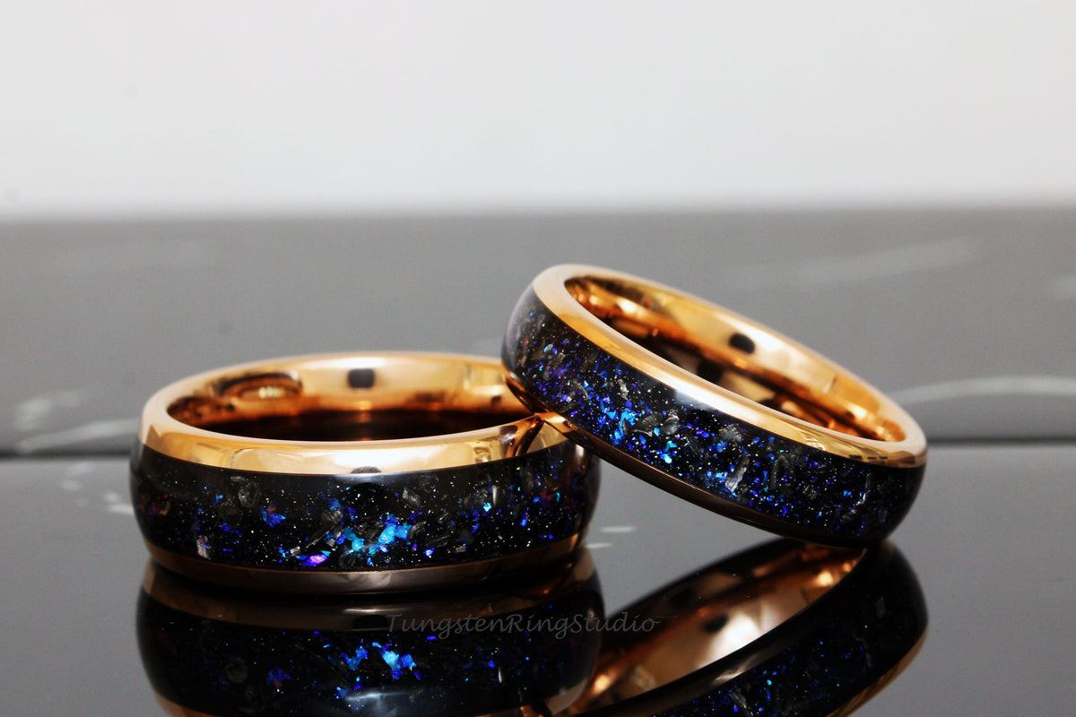 May include: Two matching tungsten carbide rings with a black inlay and a rose gold band. The inlay has a sparkly blue and black pattern.
