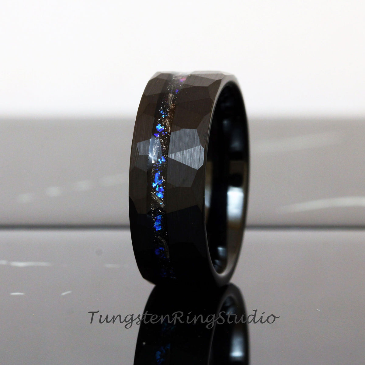 May include: Black tungsten carbide ring with a hammered finish and a blue and silver inlay. The ring is approximately 8mm wide.