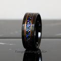 May include: A black tungsten carbide ring with a copper inlay and a blue and silver glitter inlay. The ring is on a black surface.